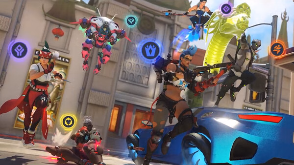 Overwatch® screenshot showing a dynamic battle scene with multiple heroes in action, each marked by colorful icons, against a city backdrop.