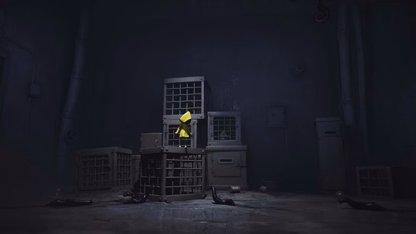 Little Nightmares screenshot: A small figure in a yellow raincoat stands on a stack of cages in a dimly lit, eerie room.