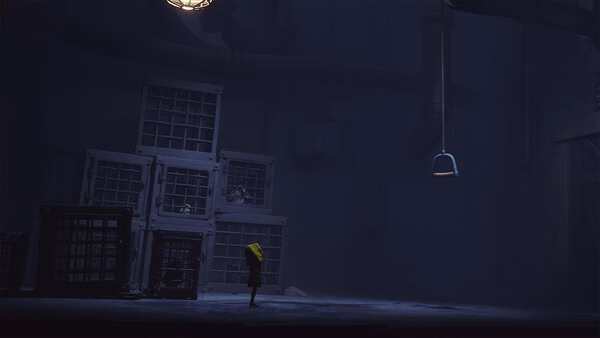 Screenshot from Little Nightmares showing a small figure in a yellow raincoat standing near stacked cages in a dimly lit room.