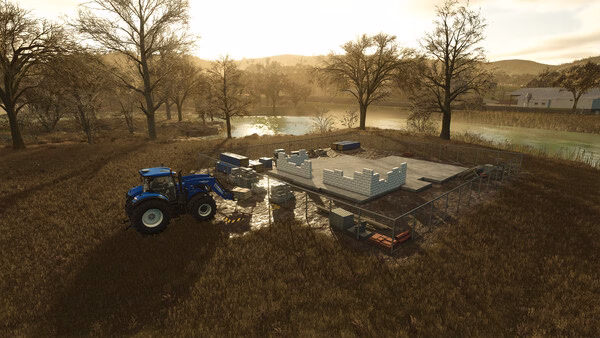 Farming Simulator 25 screenshot: A blue tractor beside a partially built structure on a farm, surrounded by trees and a river.