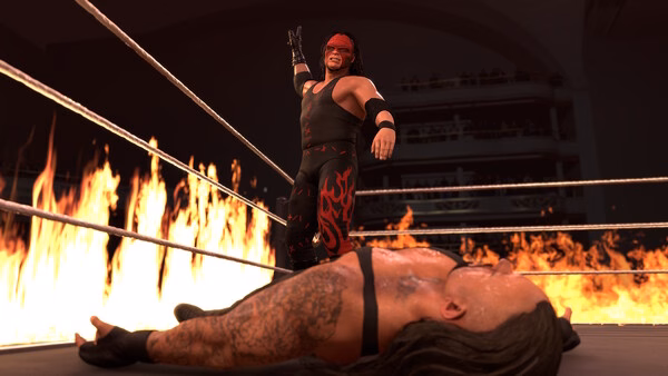 WWE 2K26 screenshot: A wrestler in a black and red outfit stands triumphantly over a fallen opponent in a ring surrounded by flames.