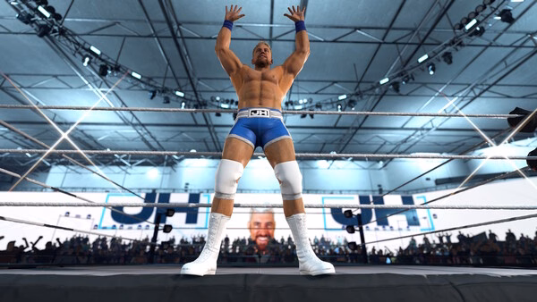 WWE 2K26 screenshot: Wrestler in blue trunks and white boots stands triumphantly in the ring, arms raised, with a cheering crowd behind.